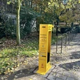 Gelbe Fahrradservice-Station von ADAC in herbstlicher Umgebung mit Bäumen und Laub auf dem Boden.