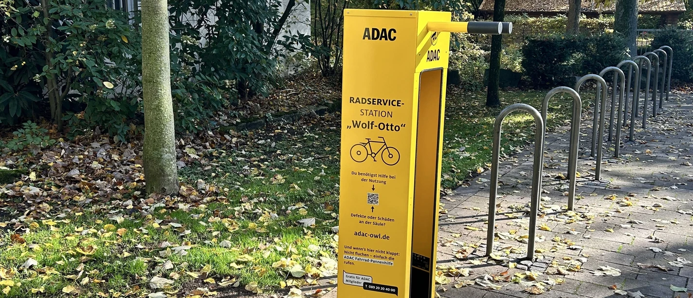 Gelbe Fahrradservice-Station von ADAC in herbstlicher Umgebung mit Bäumen und Laub auf dem Boden.