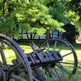 Rossmühle Oberbauerschaft Alte hölzerne Wagenräder liegen unter Bäumen, mit einem Fachwerkhaus und einer Scheune im Hintergrund.