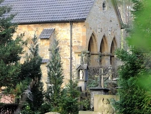 Masoleum Pfarrkirche Stockkaempen Steinernes Gebäude mit gotischen Fenstern, umgeben von Bäumen und historischen Grabsteinen im Vordergrund.