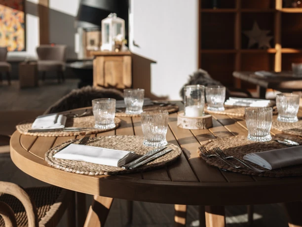 Gedeckter Holztisch in einem Restaurant mit Gläsern, Kamin und warmem Sonnenlicht