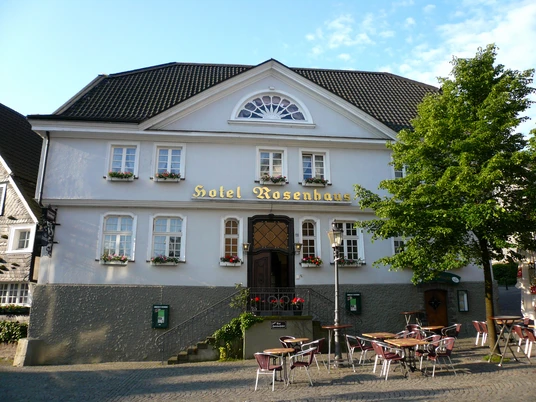 Hotel Rosenhaus in Velbert Das Hotel Rosenhaus in Velbert, ein historisches Gebäude, umgeben von Tischen auf einem gepflasterten Platz.