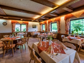 Gastraum mit gedeckten Tischen und Stühlen daran. An den Fenstern gemusterte Vorhänge