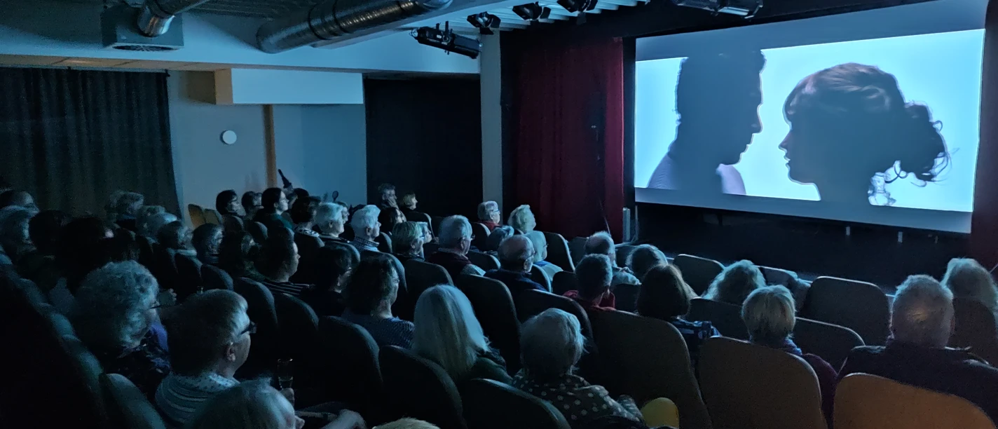 Kino Theaterstuuv.jpg Ein vollbesetztes Kino zeigt eine Projektion von zwei Personen in einem intensiven Profilmoment.