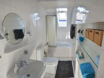 Maries B and B_Etagengästebad _M Menke.jpg Helles, modernes Badezimmer mit Badewanne, Toilette, Waschbecken und Ablagefächern im Dachgeschoss.