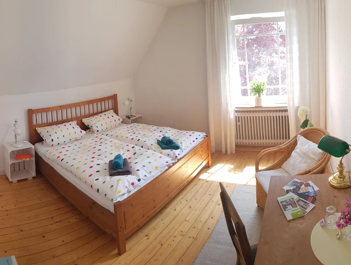 Maries B and B_Schlafraum Doppelzimmer _M Menke.jpg Zwei Einzelbetten mit bunter Bettwäsche in einem sonnigen, hellen Raum mit Holzboden und gemütlicher Einrichtung.