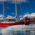 Auf dem Segelboot Rotes Segelboot gleitet durch eisiges Gewässer, umgeben von schneebedeckten Bergen und schwimmenden Eisschollen.