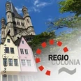 RegioColonia-Logo vor der Kirche Groß St. Martin in Köln, flankiert von bunten historischen Häusern.