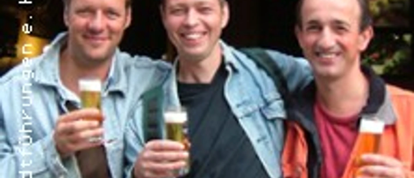 Drei Personen stehen vor einem Lokal und halten jeweils ein Glas Bier in der Hand. Sie lächeln in die Kamera.