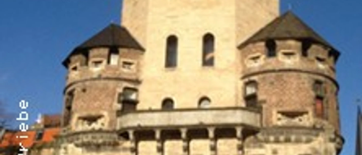 Mittelalterlicher Stadtturm mit runden Ecktürmen und Torbogen, umgeben von blauem Himmel.