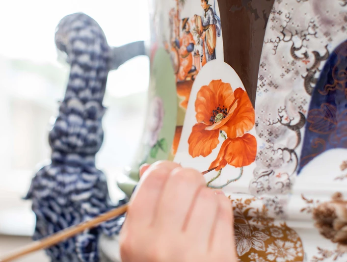 ManufakTOUR Aufglasurmalerei © MEISSEN (4).jpg Nahaufnahme einer Hand, die orangefarbene Blüten auf Porzellan mit einem Pinsel bemalt.Close-up of a hand painting orange flowers on porcelain with a brush.Detailní záběr ruky malující štětcem oranžové květy na porcelán.Zbliżenie ręki malującej pędzlem pomarańczowe kwiaty na porcelanie.Close-up van een hand die met een penseel oranjekleurige bloemen op porselein schildert.Primo piano di una mano che dipinge con un pennello fiori color arancio su porcellana.