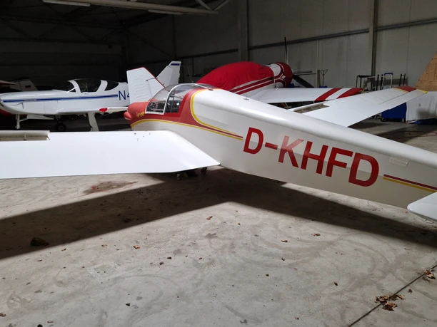 Luftsportvereinigung Meschede (Anja Weims) (23).jpg Drei Kleinflugzeuge parken in einer gut beleuchteten Halle, alle in Weiß und Rot bemalt.