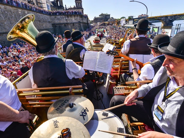 Dixielandfestival-Dixieland-Parade-2-©-Foto-Hendrik-Meyer.jpg Musiker in traditionellen Kostümen spielen Jazz auf einer fröhlichen Parade neben einem Fluss.