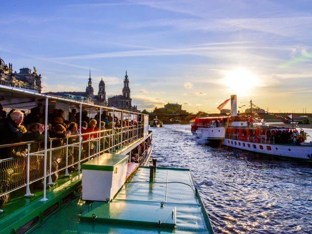 Dixielandfestival-Riverboat-Shuffle-1-©-Foto-Hendrik-Meyer.jpg Zwei historische Dampfschiffe fahren bei Sonnenuntergang auf einem Fluss voller Menschen.