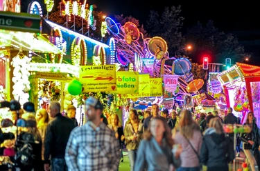 Menschen genießen lebhaftes Treiben auf einem beleuchteten Jahrmarkt, umgeben von bunten Fahrgeschäften.