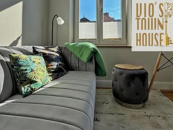 Gemütliche Sofaecke Graues Sofa mit bunten Kissen, Beistelltisch und Lampe vor Fenster in gemütlichem Raum.