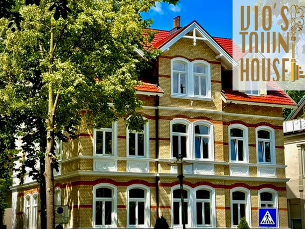 Außenansicht Historisches Stadthaus mit markanter Fassade, großen Fenstern und gepflegten Bäumen im Vordergrund.