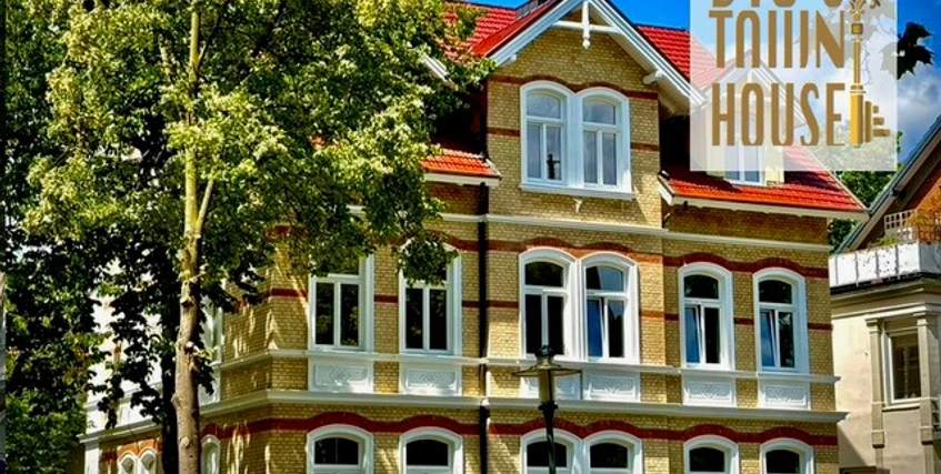 Außenansicht Historisches Stadthaus mit markanter Fassade, großen Fenstern und gepflegten Bäumen im Vordergrund.