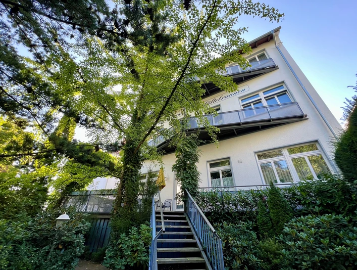 Foto Pension außen Drei-stöckiges Gebäude mit Balkonen, umgeben von Bäumen, Zugang über Treppen und Geländer.