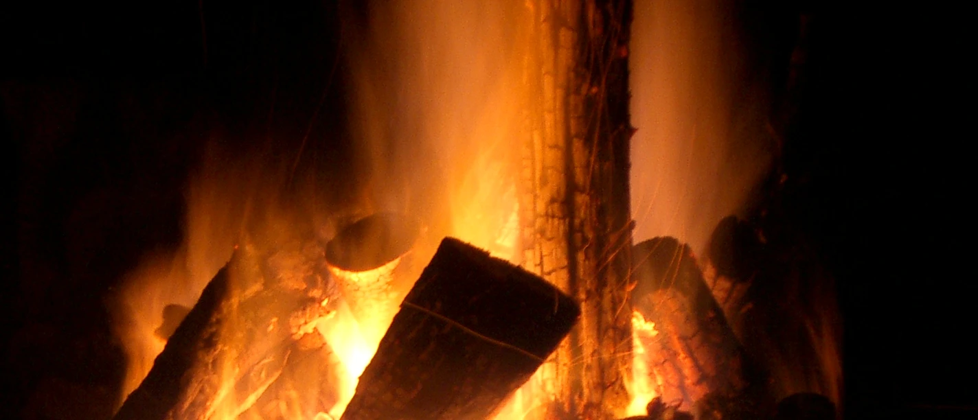 Feuer_in_SHS_©_Teutoburger_Wald_Stadt_Schloss_Holte-Stukenbrock_DPetersilie (2).JPG Lodernde Flammen verzehren Holzscheite, während Funken in der Dunkelheit aufsteigen.