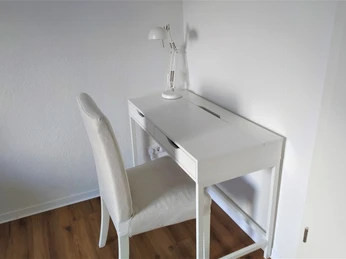 Ein schlichter weißer Schreibtisch mit passendem Stuhl, minimalistisch in einer Ecke aufgestellt.