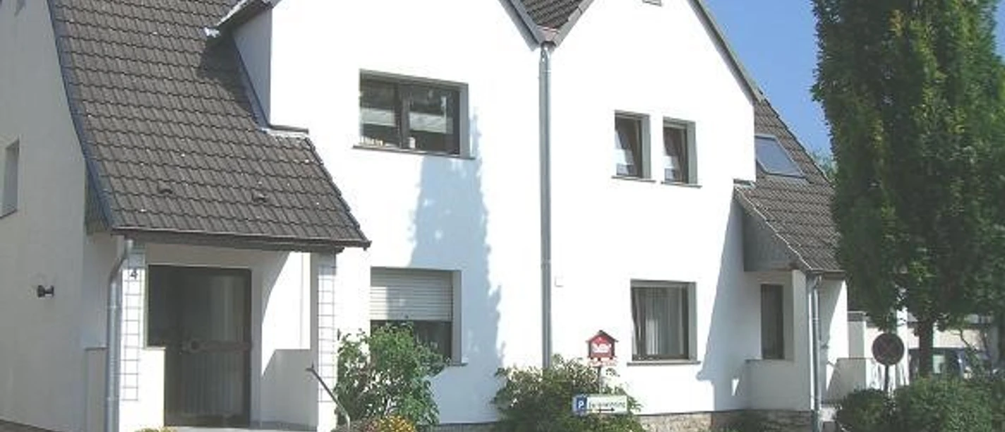 Ferienwohnung Kemper Zweistöckiges weißes Wohnhaus mit vier Giebeln, grauen Dächern und gepflegtem Vorgarten.