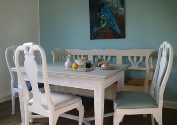 Herford_Apartment am Stiftberg_Esstisch_Niestrath (3).JPG Weißer Esstisch mit vier Stühlen und blauem Bild an der Wand, gedeckt mit Obst und Kerzen.