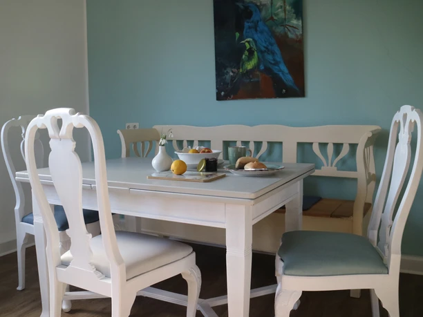 Herford_Apartment am Stiftberg_Esstisch_Niestrath (3).JPG Weißer Esstisch mit vier Stühlen und blauem Bild an der Wand, gedeckt mit Obst und Kerzen.