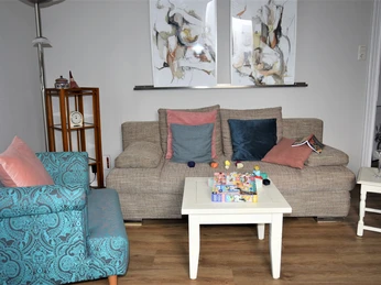Herford_Apartment am Stiftberg_WOhnbereich_Niestrath (4).JPG Wohnbereich mit beigem Sofa, blauem Sessel, Couchtisch und abstrakten Gemälden an der Wand.