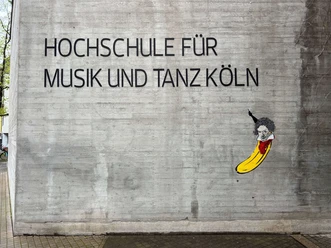 Beethoven Banana by Thomas Baumgärtel The picture shows a work of street art by Thomas Baumgärtel on the façade of the Cologne University of Music and Dance. It depicts a banana that resembles Ludwig van Beethoven in a stylized portrait. The banana is painted in bright yellow and its upper side is designed to have Beethoven's characteristic hair and facial features.