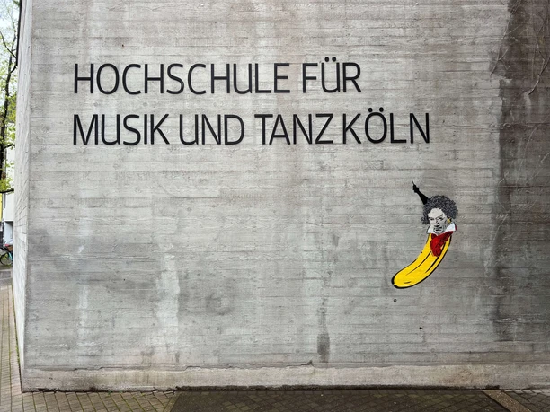 Beethoven Banana by Thomas Baumgärtel The picture shows a work of street art by Thomas Baumgärtel on the façade of the Cologne University of Music and Dance. It depicts a banana that resembles Ludwig van Beethoven in a stylized portrait. The banana is painted in bright yellow and its upper side is designed to have Beethoven's characteristic hair and facial features.