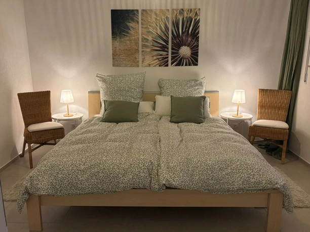 Schlafzimmer_01 Gemütliches Schlafzimmer mit Doppelbett, zwei Nachttischen und weichen Lampen in warmem Licht.