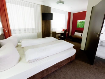 Ein modernes Hotelzimmer mit Doppelbett, Schreibtisch, Sessel und Flachbild-TV, in warmen Farben.