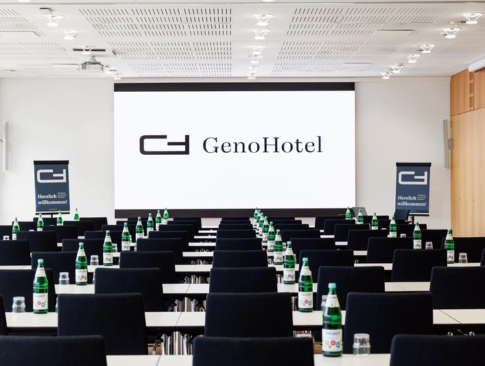 S 9 + S10 Konferenzraum mit parlamentarischer Bestuhlung und Blick auf die Leinwand mit der Aufschrift "Geno Hotel Forsbach"Conference room with parliamentary seating and a view of the screen with the inscription "Geno Hotel Forsbach"