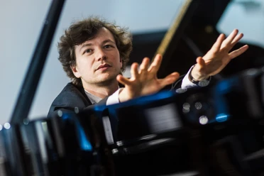Mikhail Mordvinov Pianist Mikhail Mordvinov am Flügel mit erhobenen Händen.