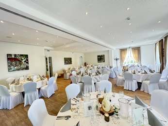 Hochzeit Kortenhof Ein lichtdurchfluteter Festsaal mit runden Tischen, elegant eingedeckt für eine Hochzeitsfeier.