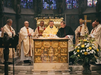 Ein Gottesdienst mit mehreren Geistlichen, die um einen prunkvollen Altar in einer festlichen Kirche versammelt sind.