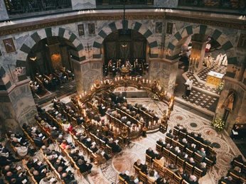 Besucher nehmen an einer feierlichen Messe im Aachener Dom teil, beleuchtet von warmem Kerzenlicht.