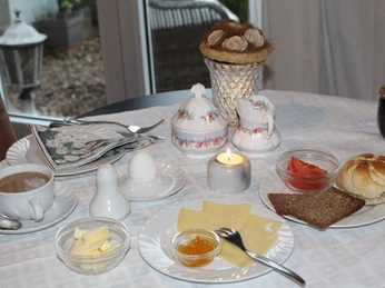 Frühstück Frühstückstisch mit Kaffee, Eiern, Käse, Brötchen und Kerze, umgeben von Teller und Geschirr.