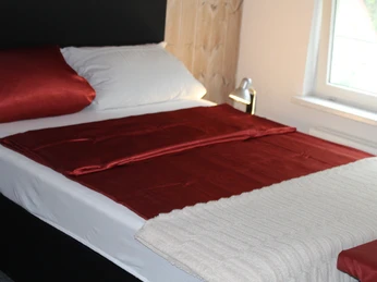 Schlafzimmer, Boxspringbett Modernes Schlafzimmer mit einem Boxspringbett, roten Bettdecken und natürlichem Licht durch ein Fenster.