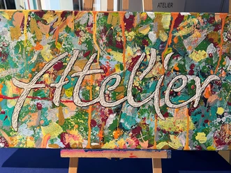 Atelier Vielseitig gestaltete Leinwand mit dem Schriftzug "Atelier" vor einer Staffelei, farbenreich bemalt.