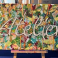 Atelier Vielseitig gestaltete Leinwand mit dem Schriftzug "Atelier" vor einer Staffelei, farbenreich bemalt.