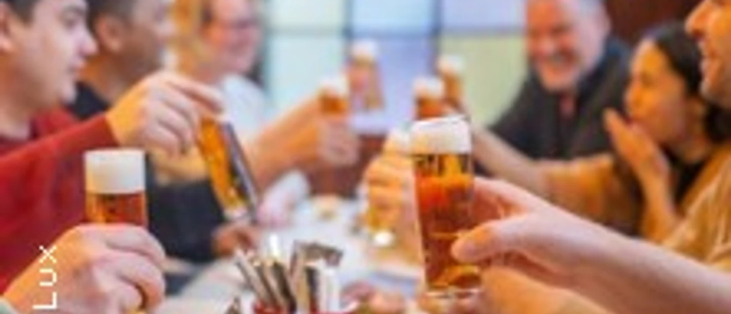 Eine Gruppe von Menschen prostet sich mit kleinen Biergläsern an einem Tisch in einem geselligen Umfeld zu.