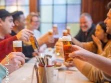 Eine Gruppe von Menschen prostet sich mit kleinen Biergläsern an einem Tisch in einem geselligen Umfeld zu.