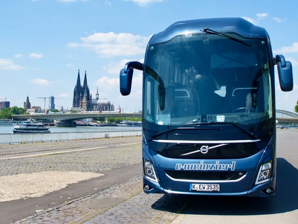 Volvo.Vorne2.jpeg Blauer Bus mit der Aufschirft "e-Weinzierl" steht am Rheinufer, mit Kölner Dom im Hintergrund