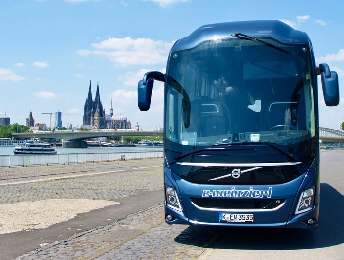 Volvo.Vorne2.jpeg Blauer Bus mit der Aufschirft "e-Weinzierl" steht am Rheinufer, mit Kölner Dom im HintergrundBlue bus with the sign "e-Weinzierl" stands on the banks of the Rhine, with Cologne Cathedral in the background