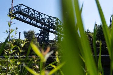 Wohnmobilstellplatz Landschaftspark Duisburg-Nord Das gezeigte Bild zeigt einen eindrucksvollen alten Industriekran, umgeben von grüner Natur.