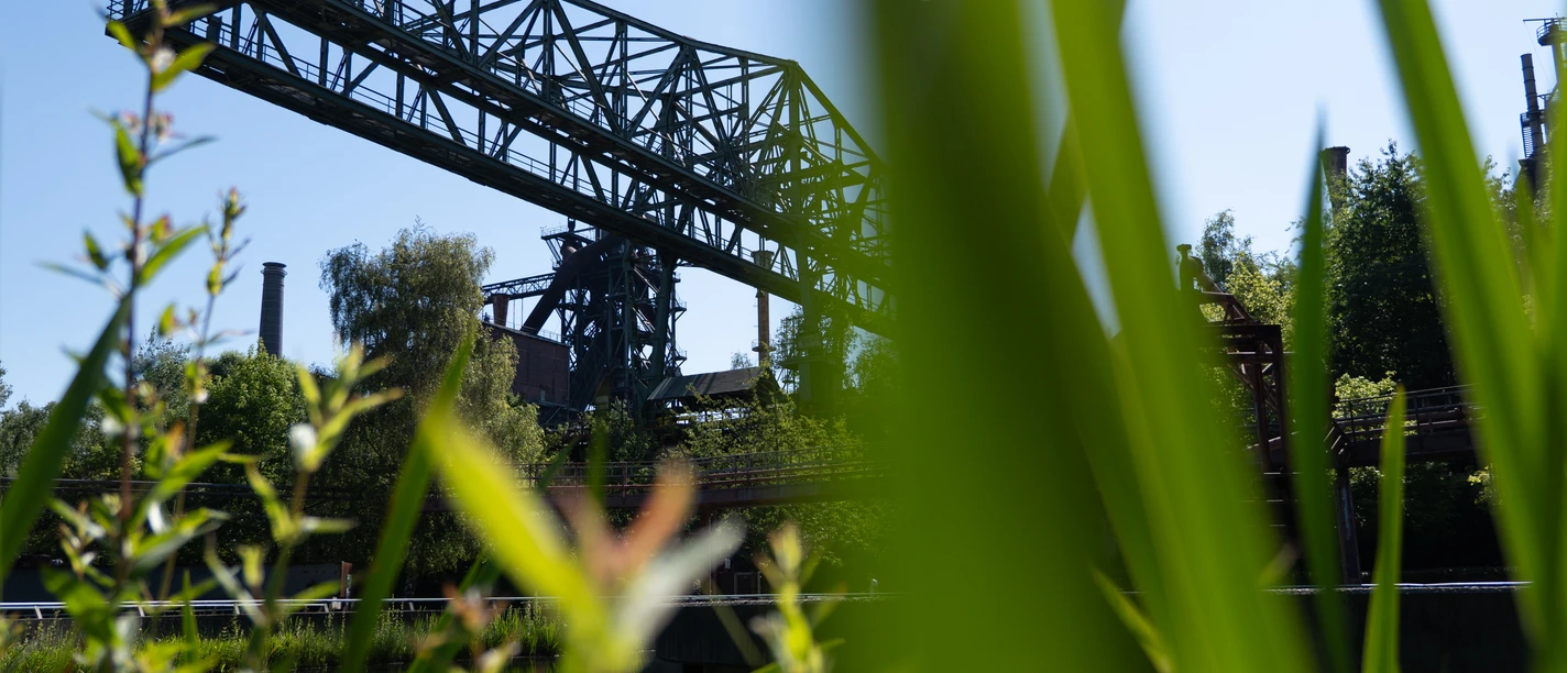 Wohnmobilstellplatz Landschaftspark Duisburg-Nord Das gezeigte Bild zeigt einen eindrucksvollen alten Industriekran, umgeben von grüner Natur.