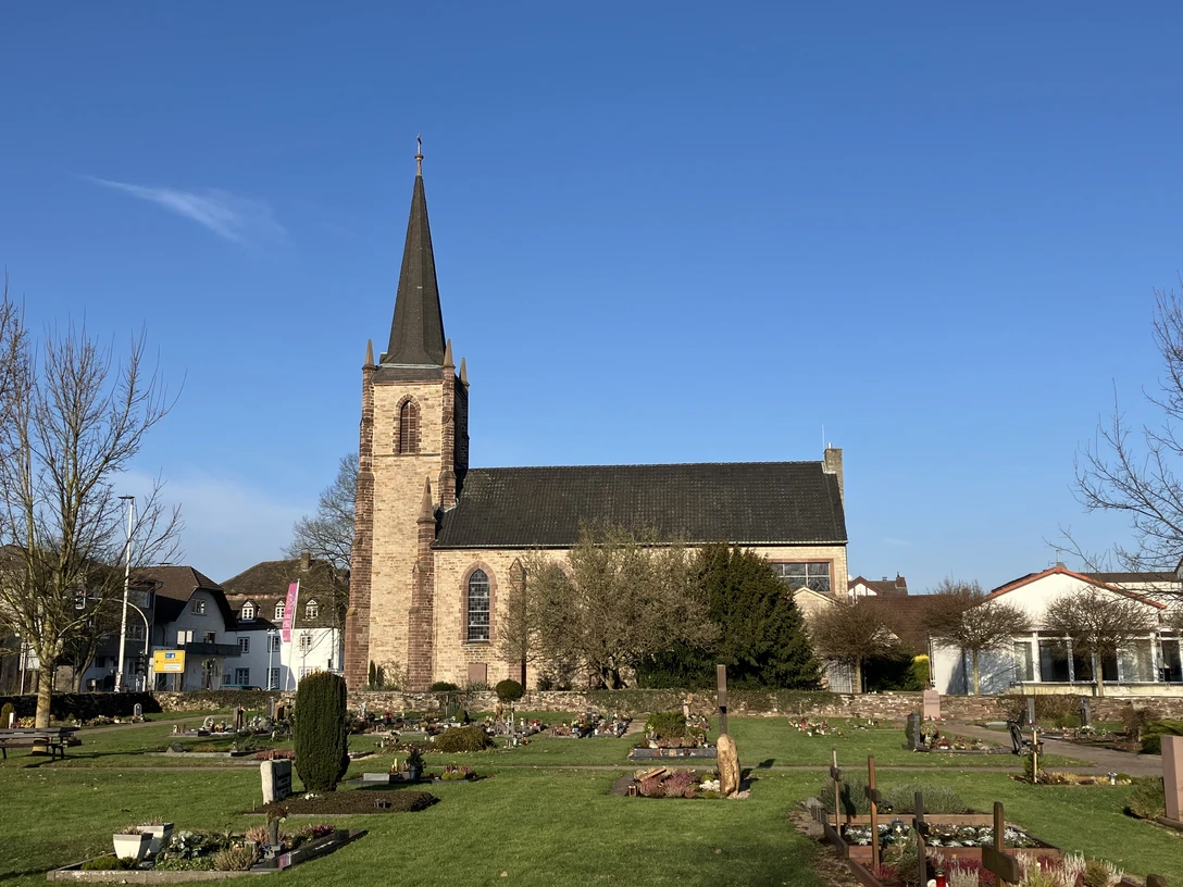 Evangelische Kirche Beverungen mit markantem Turm, umgeben von gepflegtem Friedhof und Bäumen.