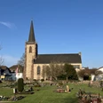 Evangelische Kirche Beverungen mit markantem Turm, umgeben von gepflegtem Friedhof und Bäumen.